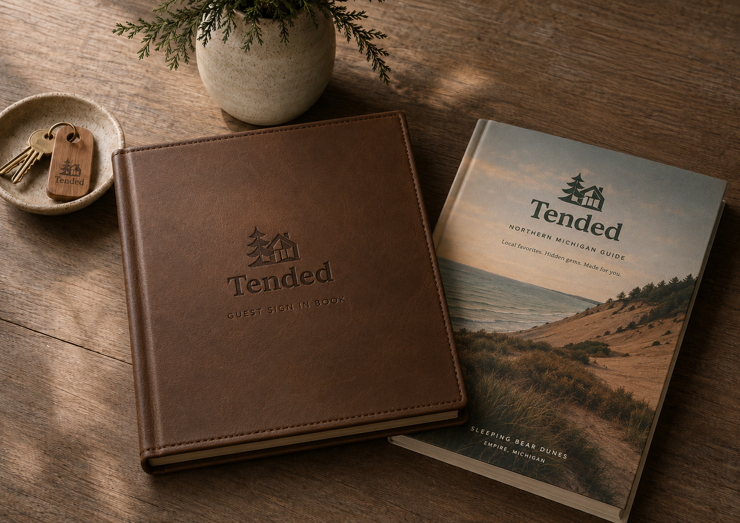 Tended-branded leather guest sign-in book and Northern Michigan guide book on a wood table with keys and greenery.